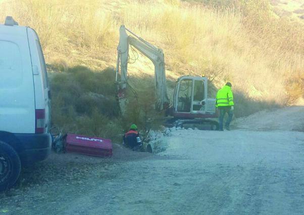 Miniexcavadora y operarios trabajando en el talud junto al camino del Realejo, con una furgoneta de obra en primer plano.