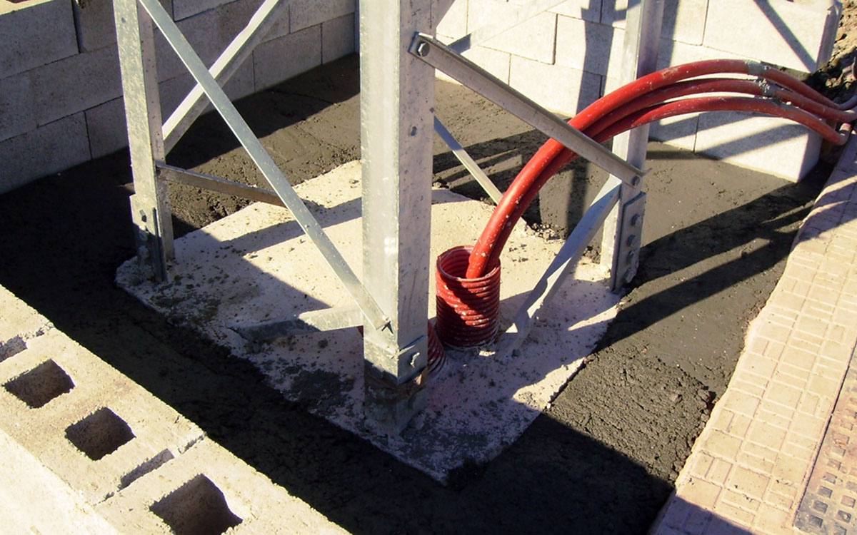 Tubos corrugados rojos de canalización eléctrica que salen de la cimentación de un apoyo metálico de celosía.