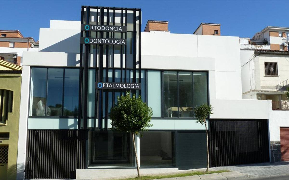 Edificio de consultas médicas con fachada blanca, carpinterías oscuras y celosía vertical en la entrada.
