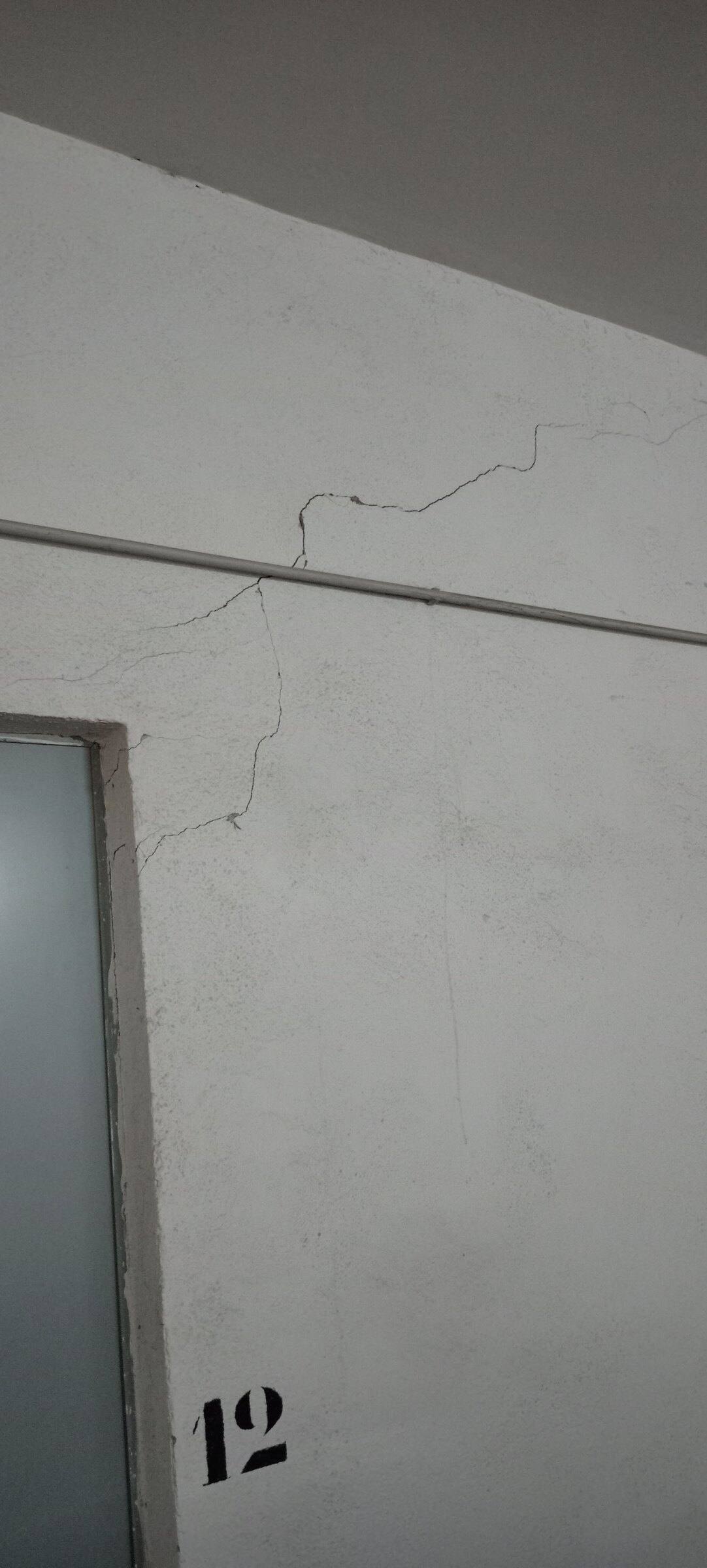 Grieta escalonada que parte de la esquina de una puerta en un trastero numerado.