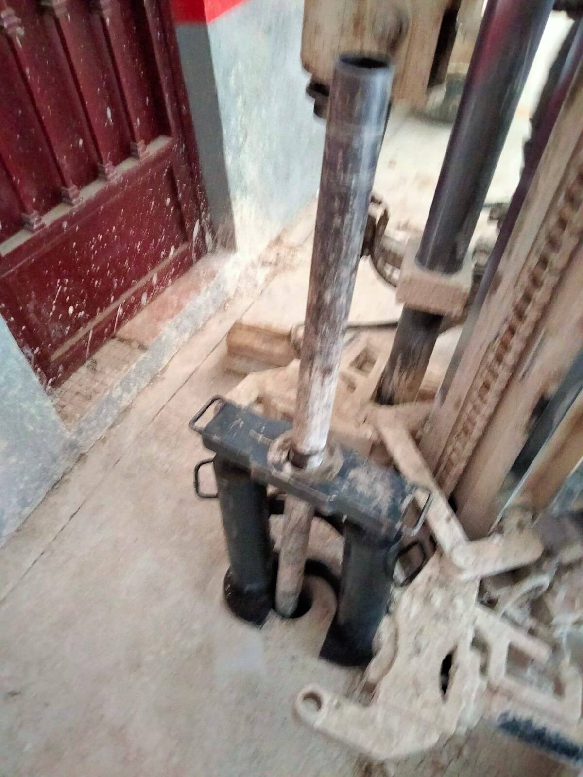 Mástil de perforación apoyado en el suelo junto a una puerta, atravesando el pavimento interior.