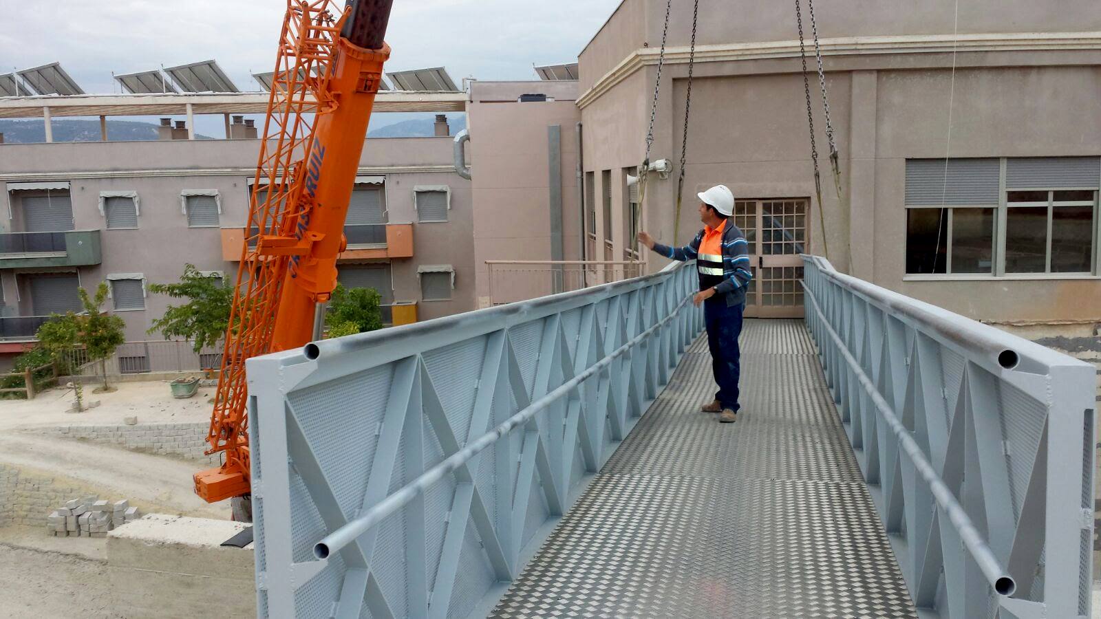 Pasarela metálica peatonal colgada de una grúa autopropulsada, con un técnico de Toledano con casco sobre el tablero.