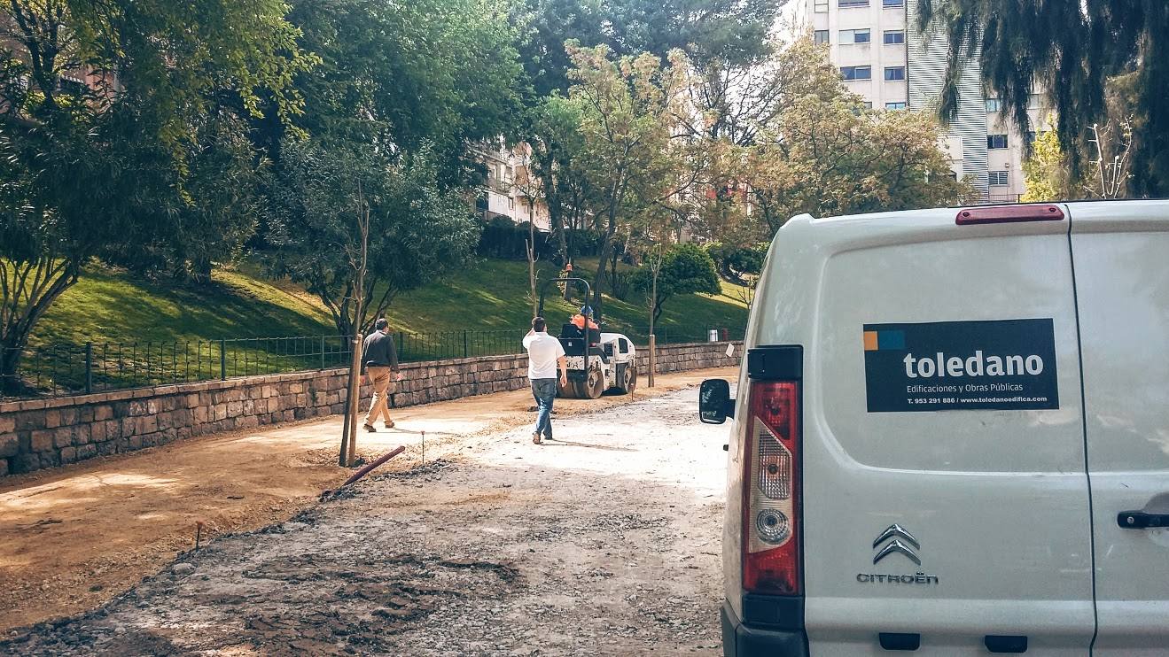 Paseo arbolado en obras con un compactador al fondo y una furgoneta rotulada de Toledano en primer plano.