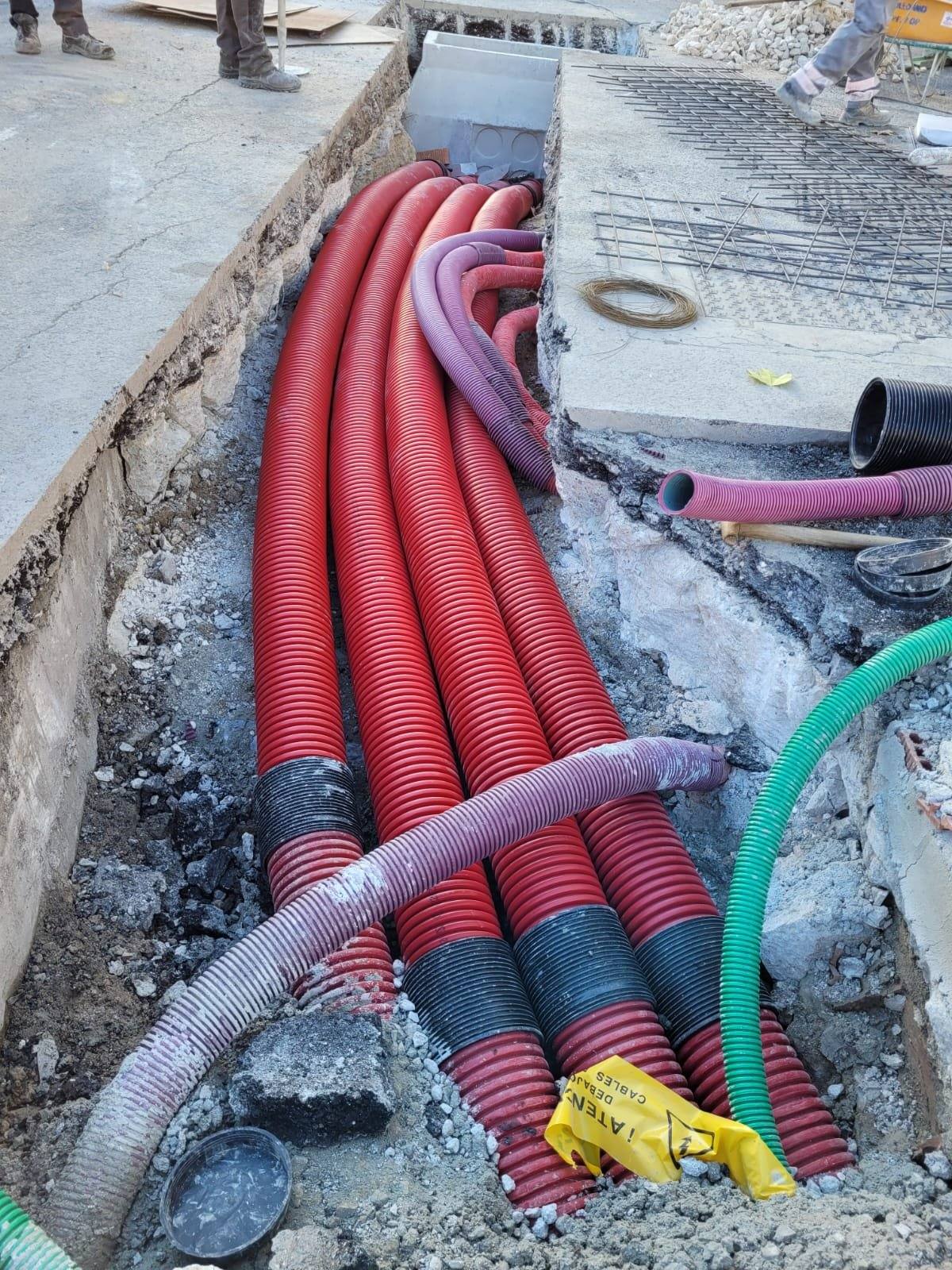 Haz de tubos corrugados rojos que gira en el fondo de la excavación, entre restos de pavimento y otras conducciones existentes.