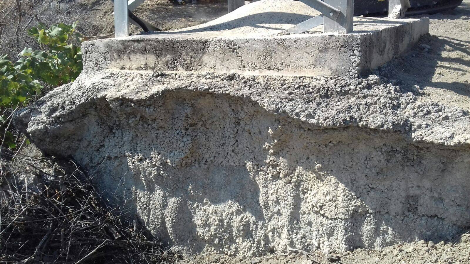 Zapata de hormigón de un apoyo al borde de un talud erosionado, con el terreno descarnado bajo el canto de la cimentación.