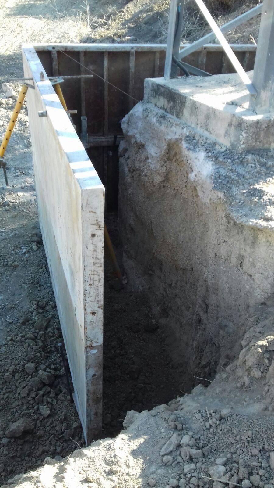 Viga de hormigón recién desencofrada junto a la zapata del apoyo, con la zanja entre ambas y un encofrado de madera al fondo.