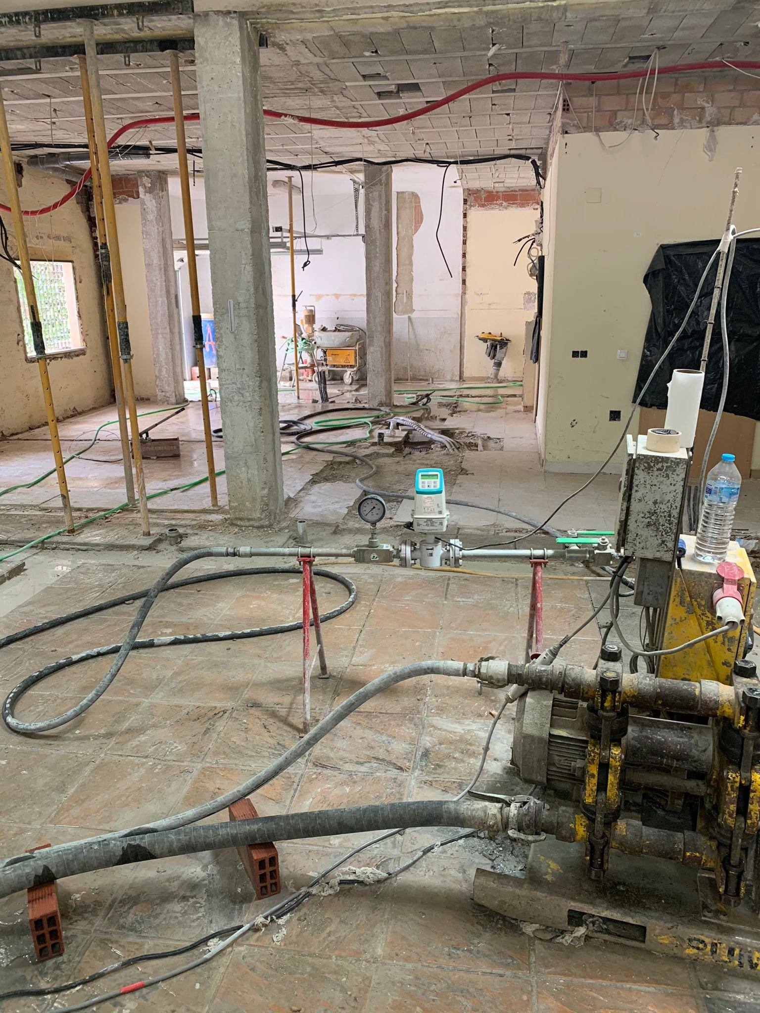 Bomba de inyección y mangueras extendidas por una planta baja diáfana con pilares, con el pavimento retirado.